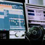 Close-up of a professional music studio setup featuring an amplifier and headphones with digital audio workstations in the background.